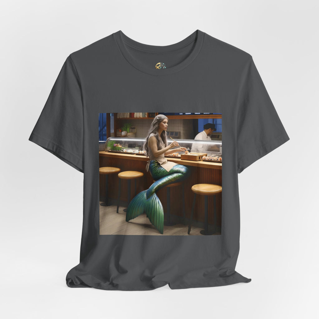 Asphalt grey T-shirt featuring a graphic of a mermaid wearing a chef’s apron sitting at a sushi bar and eating sushi, with a chef behind the counter