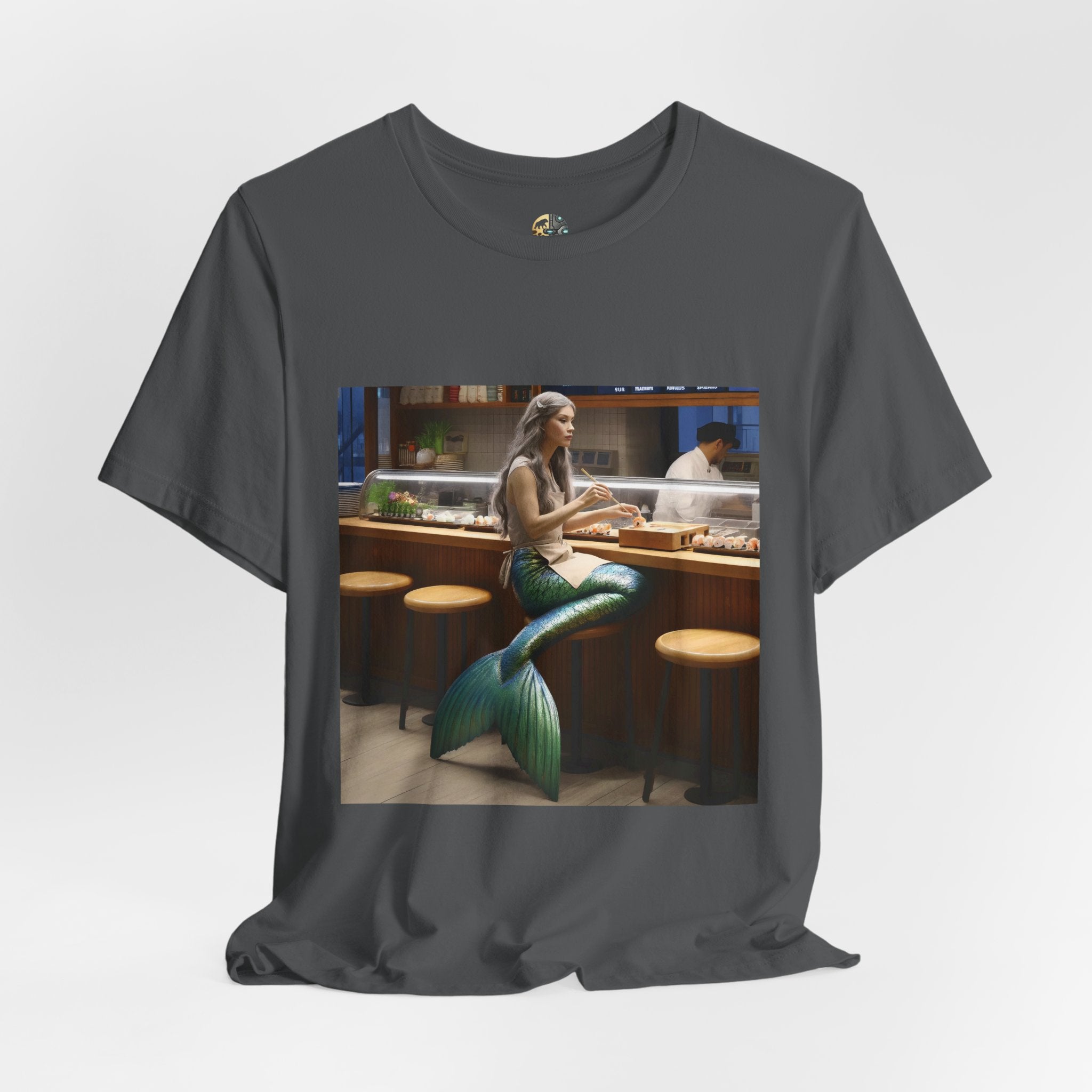 Asphalt grey T-shirt featuring a graphic of a mermaid wearing a chef’s apron sitting at a sushi bar and eating sushi, with a chef behind the counter