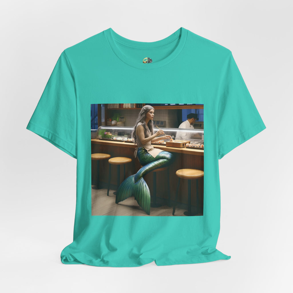Teal T-shirt featuring a graphic of a mermaid wearing a chef’s apron sitting at a sushi bar and eating sushi, with a chef behind the counter
