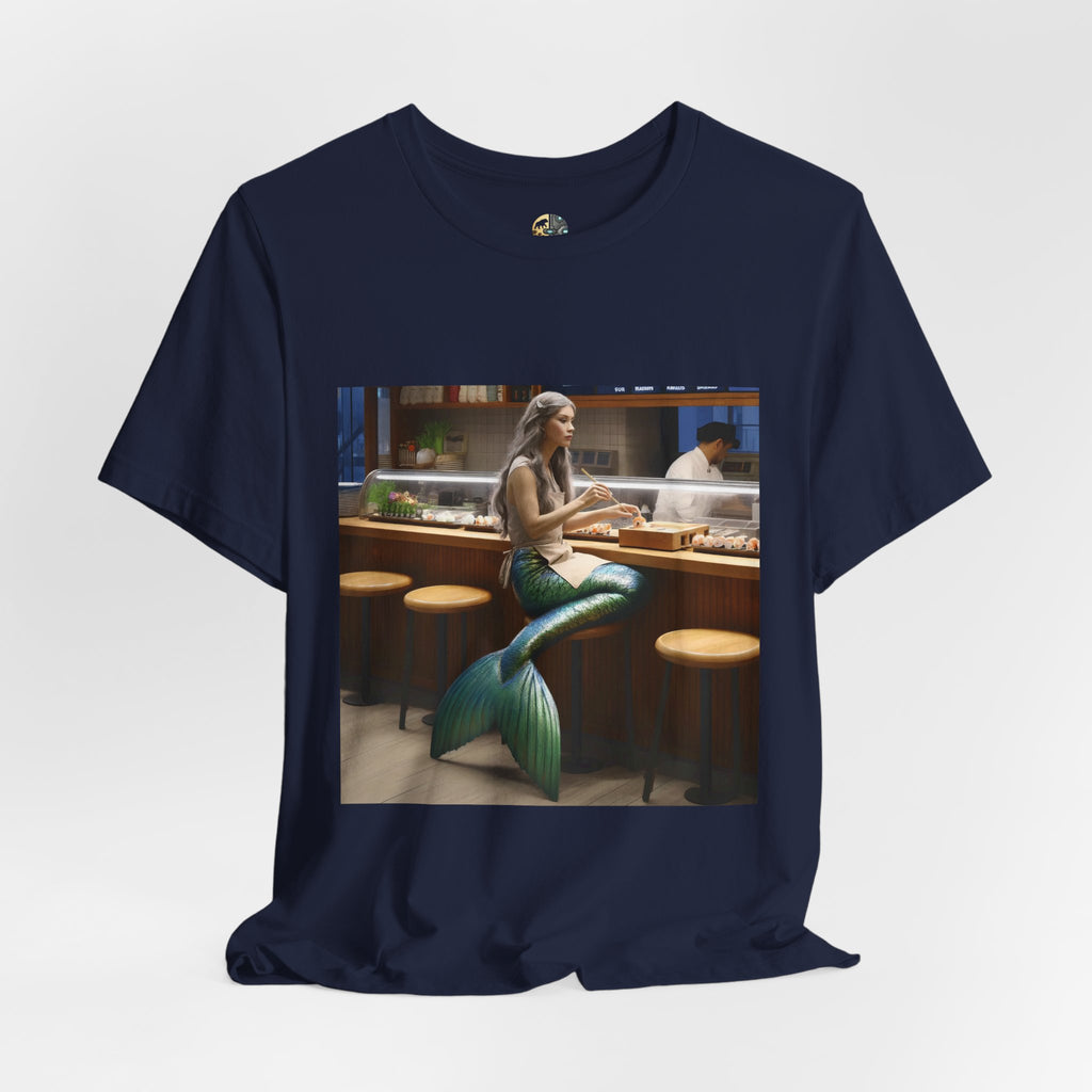 Navy blue T-shirt featuring a graphic of a mermaid wearing a chef’s apron sitting at a sushi bar and eating sushi, with a chef behind the counter