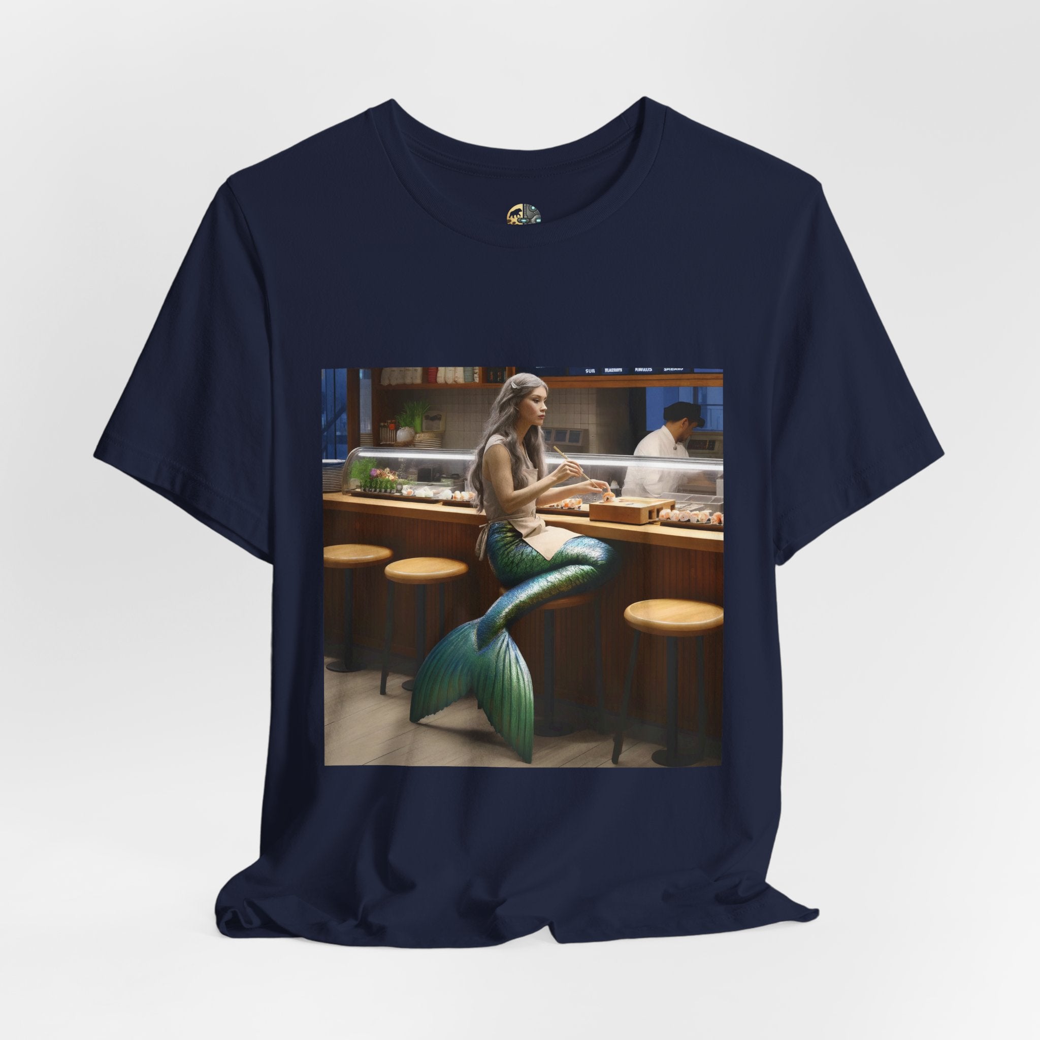 Navy blue T-shirt featuring a graphic of a mermaid wearing a chef’s apron sitting at a sushi bar and eating sushi, with a chef behind the counter