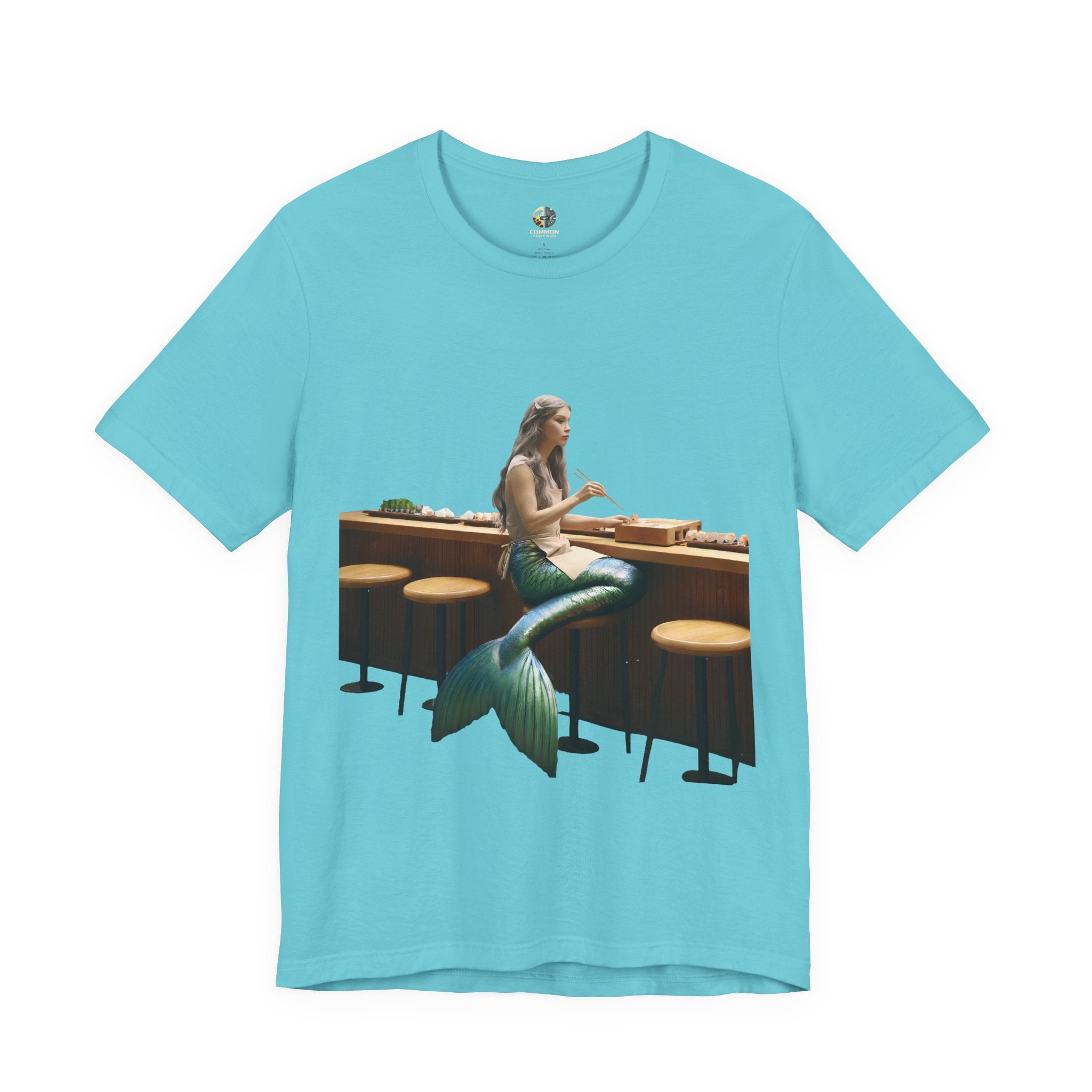 Turquoise T-shirt with graphic of a mermaid wearing a chef’s apron sitting at a sushi bar and eating sushi with chopsticks