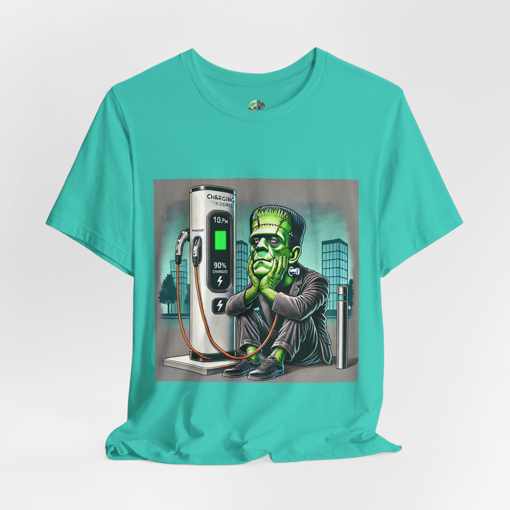 Teal T-shirt featuring a graphic of Frankenstein’s monster sitting at an electric charging station, plugged in and waiting for the charge to complete, with office buildings in the background