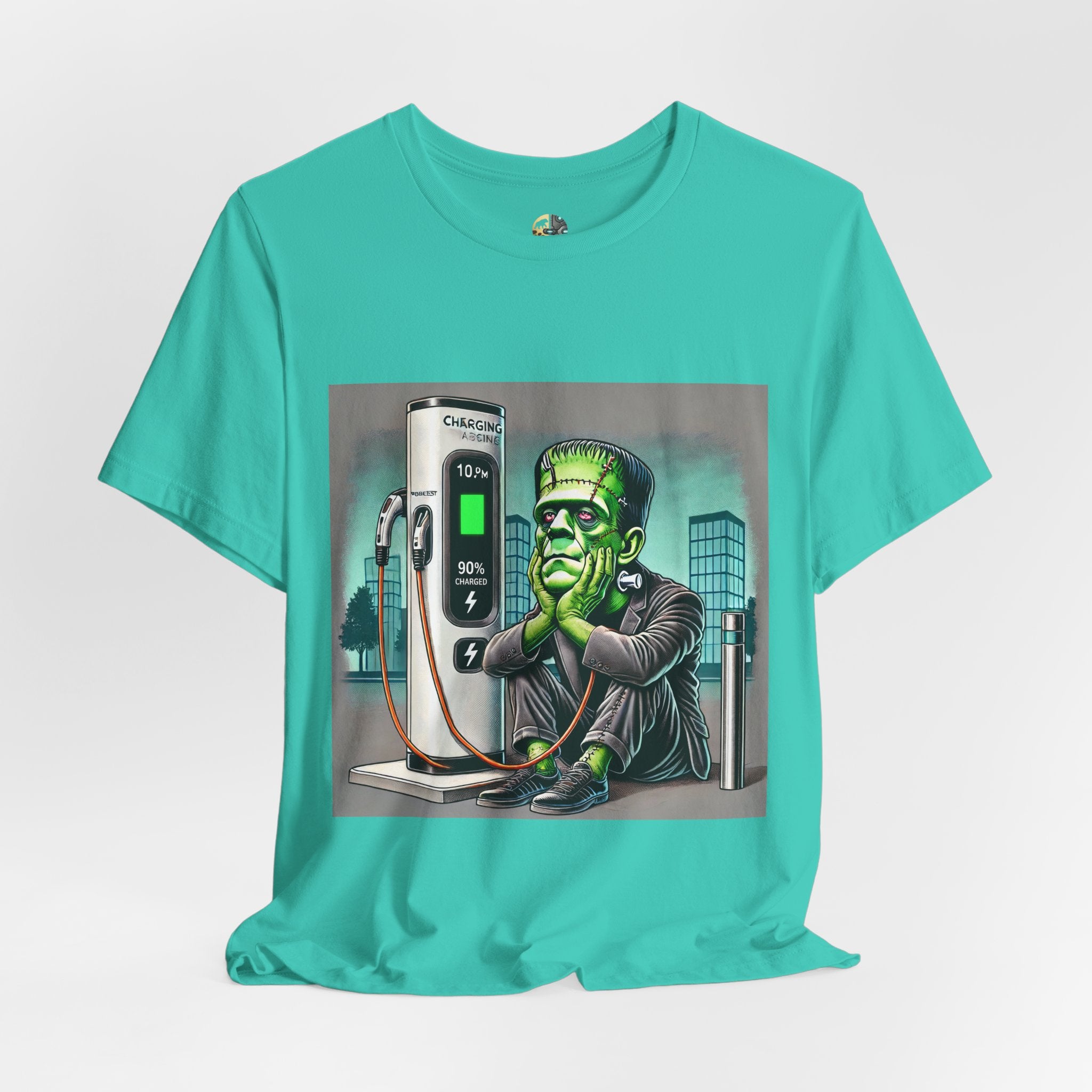Teal T-shirt featuring a graphic of Frankenstein’s monster sitting at an electric charging station, plugged in and waiting for the charge to complete, with office buildings in the background