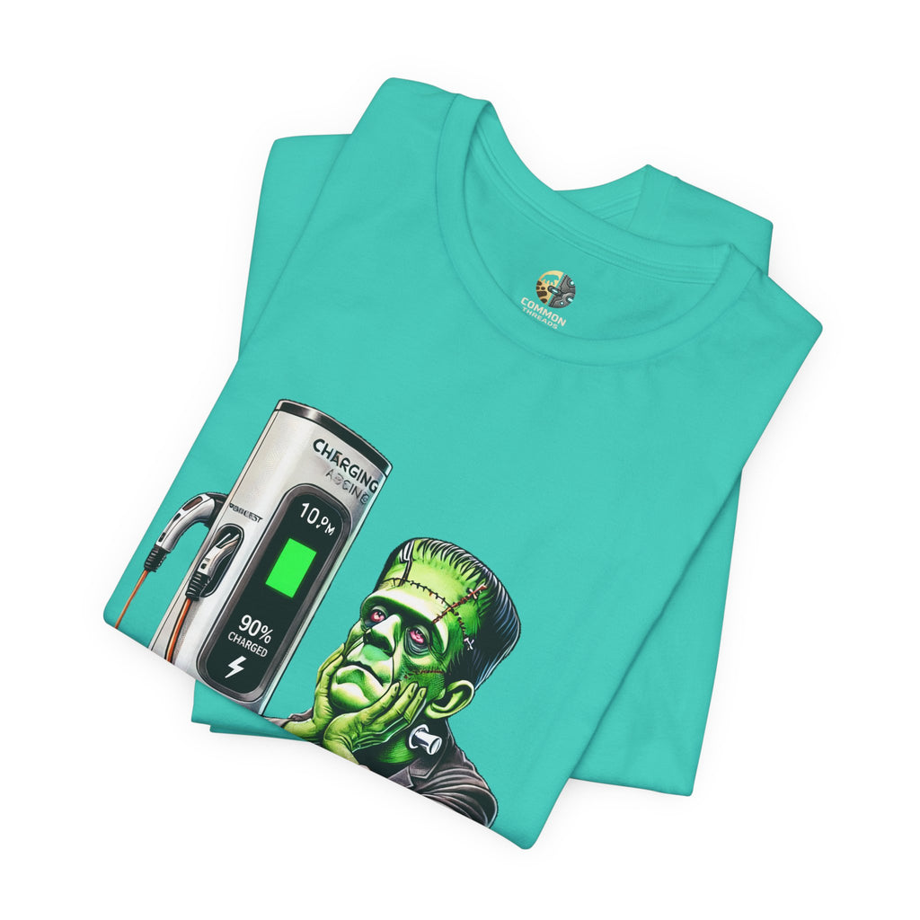 Folded teal T-shirt featuring a graphic of Frankenstein’s monster sitting at an electric charging station, plugged in and waiting for the charge to complete