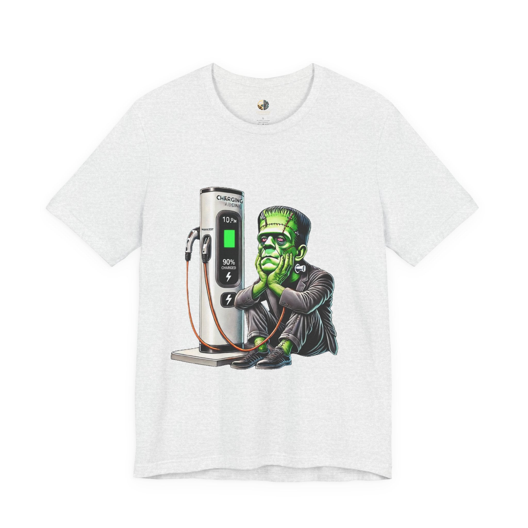 Ash color T-shirt featuring a graphic of Frankenstein’s monster sitting at an electric charging station, plugged in and waiting for the charge to complete