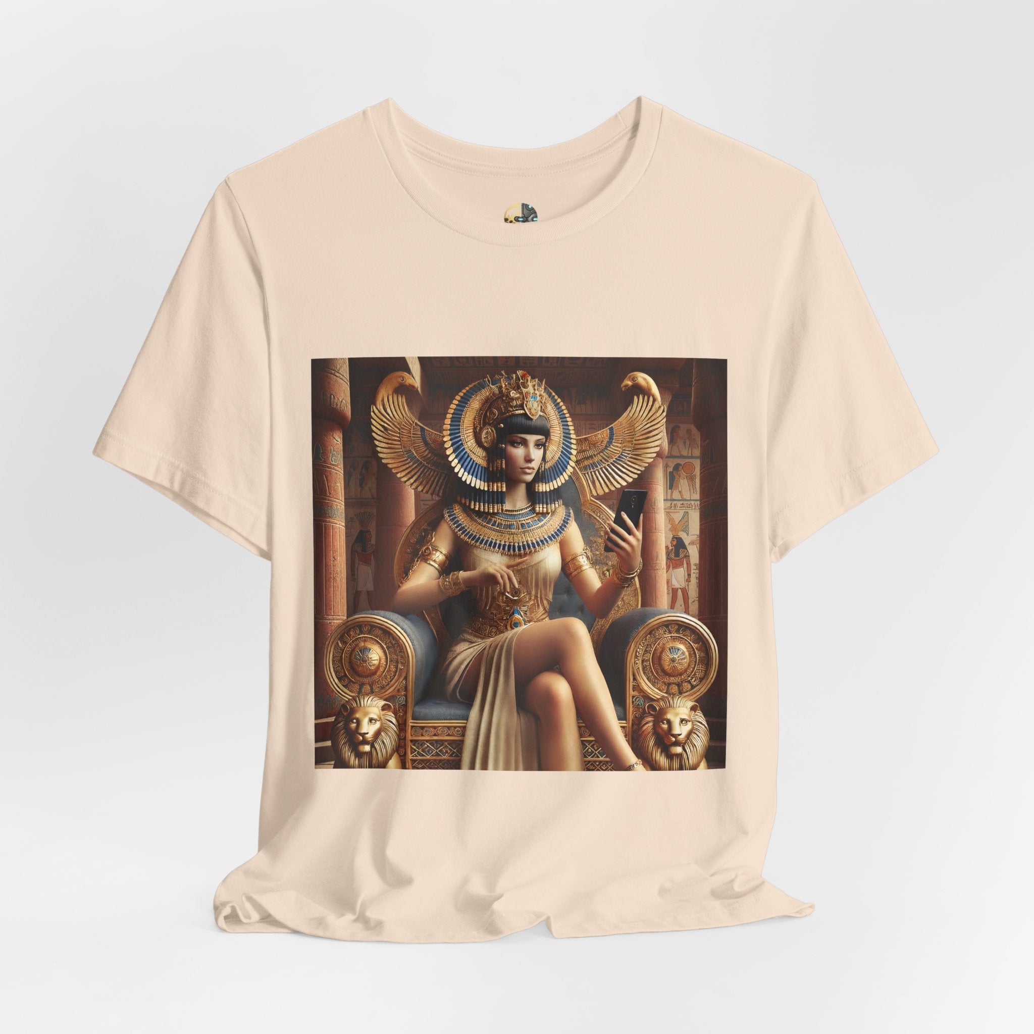 Soft creme T-shirt featuring a graphic of Cleopatra wearing an ornate headdress and gold jewelry, seated on a throne and holding a smartphone for a selfie, with temple architecture in the background