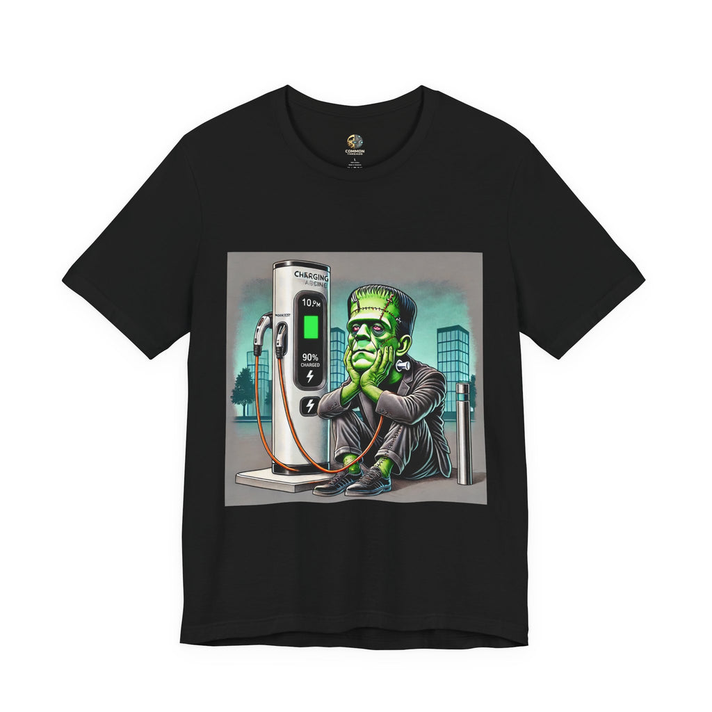Black T-shirt featuring a graphic of Frankenstein’s monster sitting at an electric charging station, plugged in and waiting for the charge to complete, with office buildings in the background