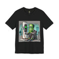Black T-shirt featuring a graphic of Frankenstein’s monster sitting at an electric charging station, plugged in and waiting for the charge to complete, with office buildings in the background