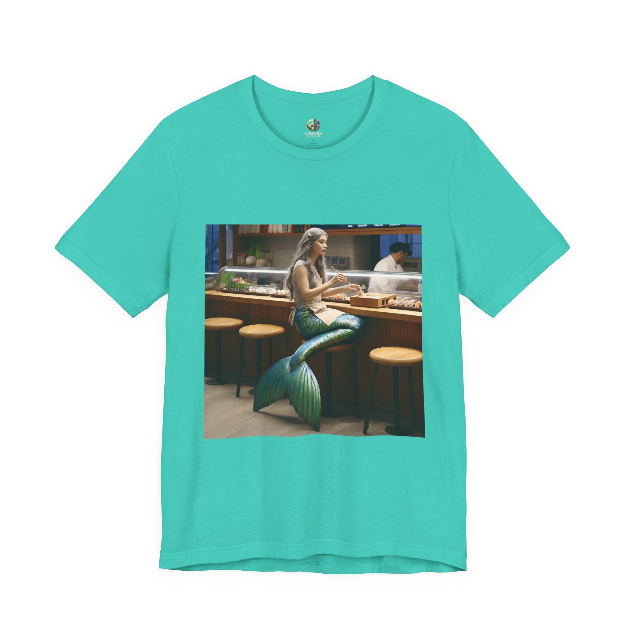 Teal T-shirt featuring a graphic of a mermaid wearing a chef’s apron sitting at a sushi bar and eating sushi, with a chef behind the counter