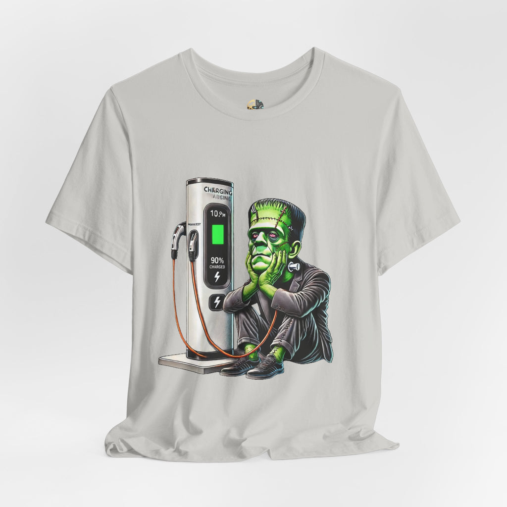 Silver T-shirt featuring a graphic of Frankenstein’s monster sitting at an electric charging station, plugged in and waiting for the charge to complete