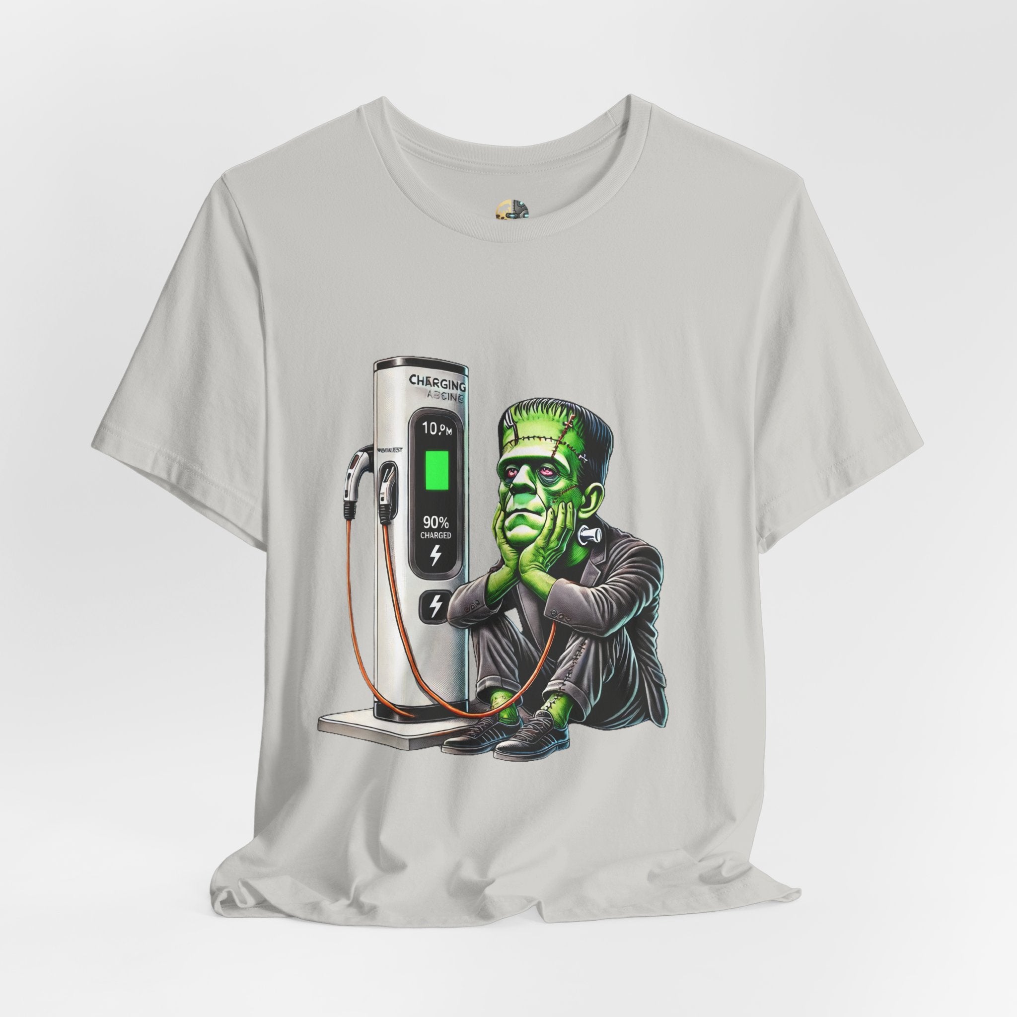 Silver T-shirt featuring a graphic of Frankenstein’s monster sitting at an electric charging station, plugged in and waiting for the charge to complete