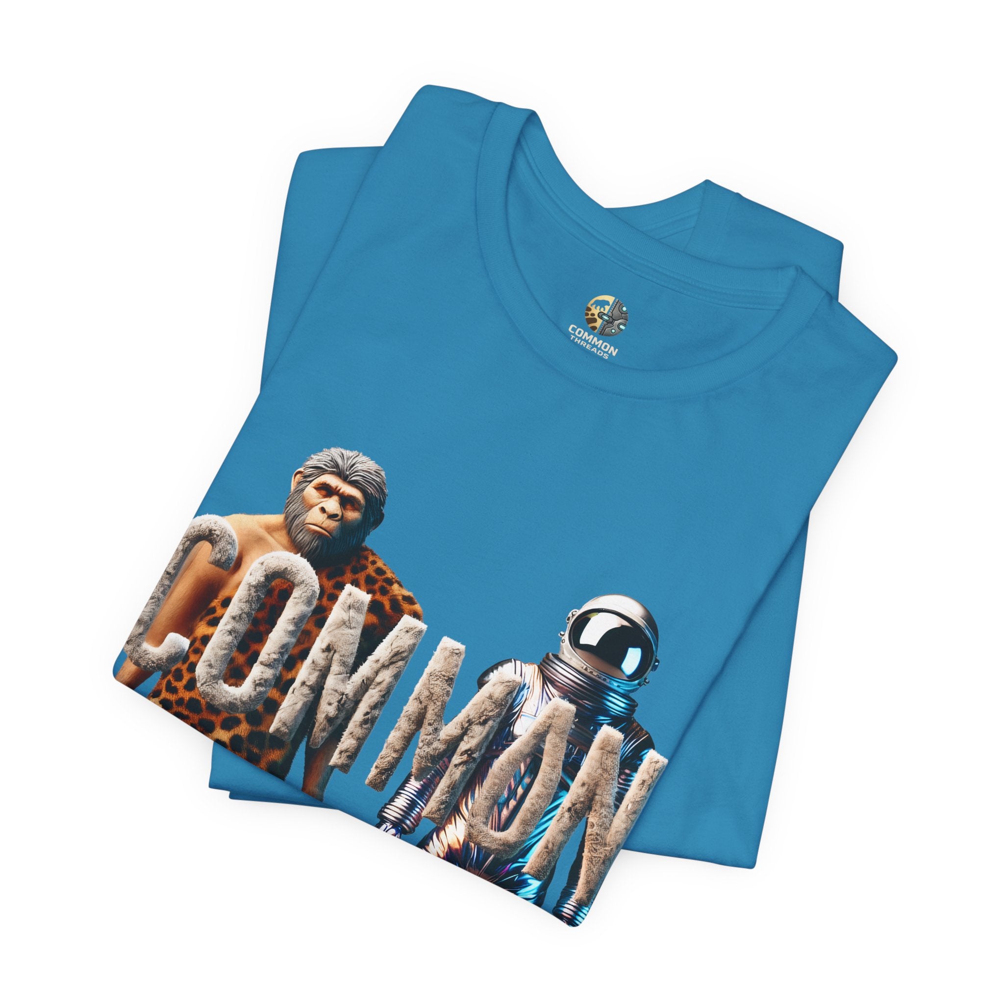 Folded aqua blue T-shirt featuring a graphic of a caveman in animal pelts standing beside a chrome-plated astronaut, with the text ‘Common Threads‘