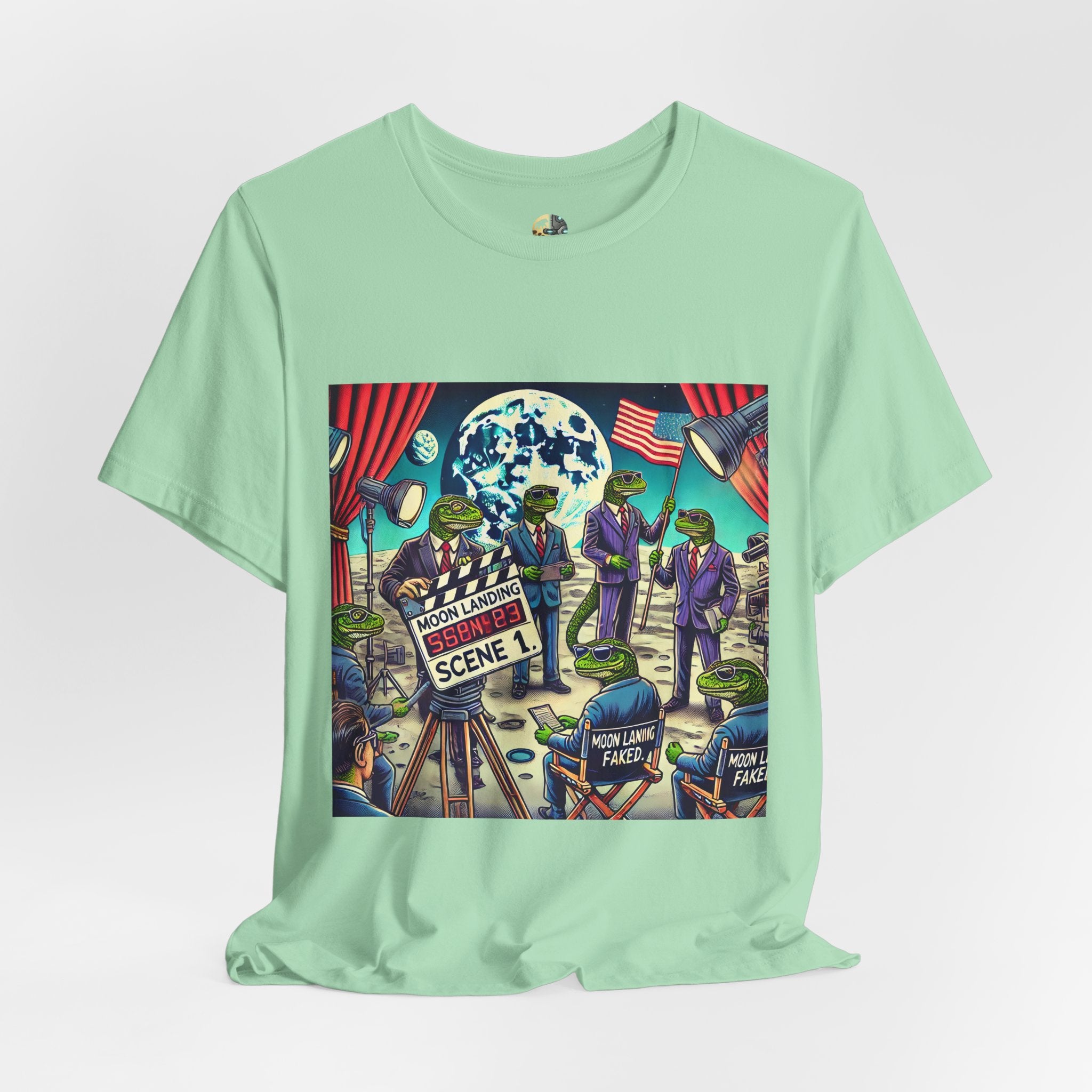 Mint green T-shirt featuring a graphic of lizard people in suits on a movie set staging a moon landing scene, with studio lights and a clapperboard