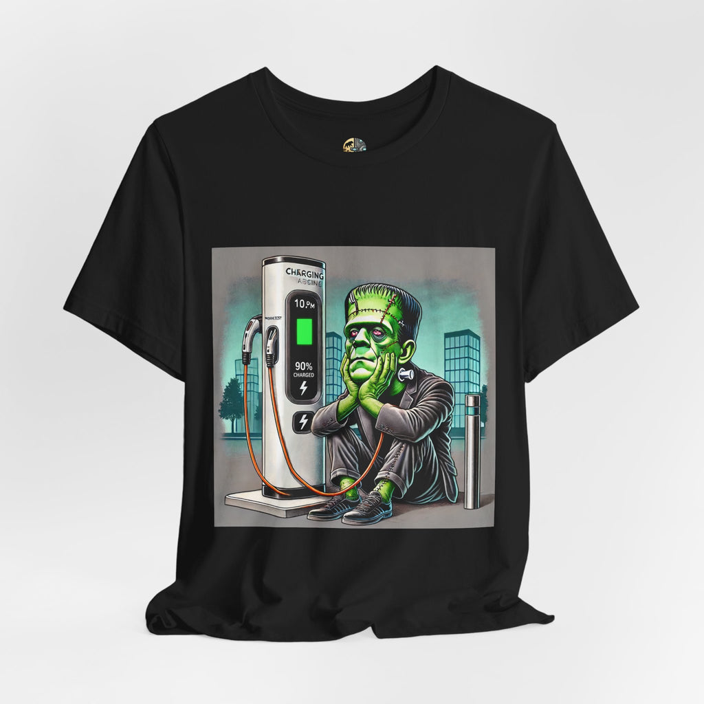Black T-shirt featuring a graphic of Frankenstein’s monster sitting at an electric charging station, plugged in and waiting for the charge to complete, with office buildings in the background