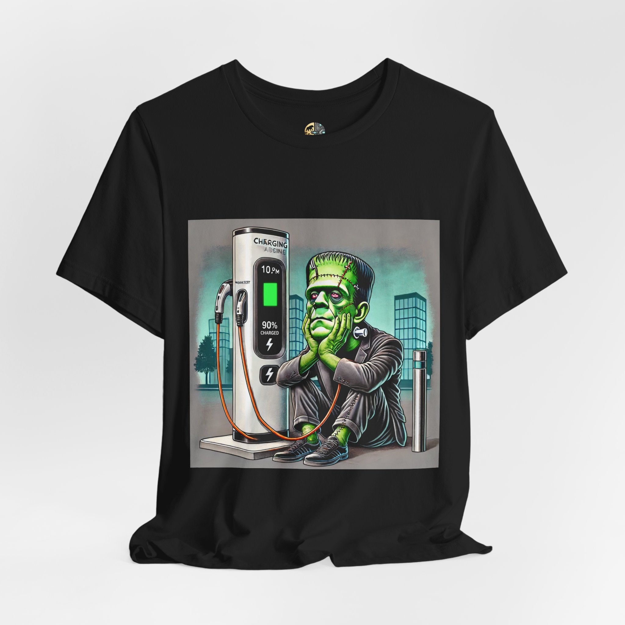 Black T-shirt featuring a graphic of Frankenstein’s monster sitting at an electric charging station, plugged in and waiting for the charge to complete, with office buildings in the background