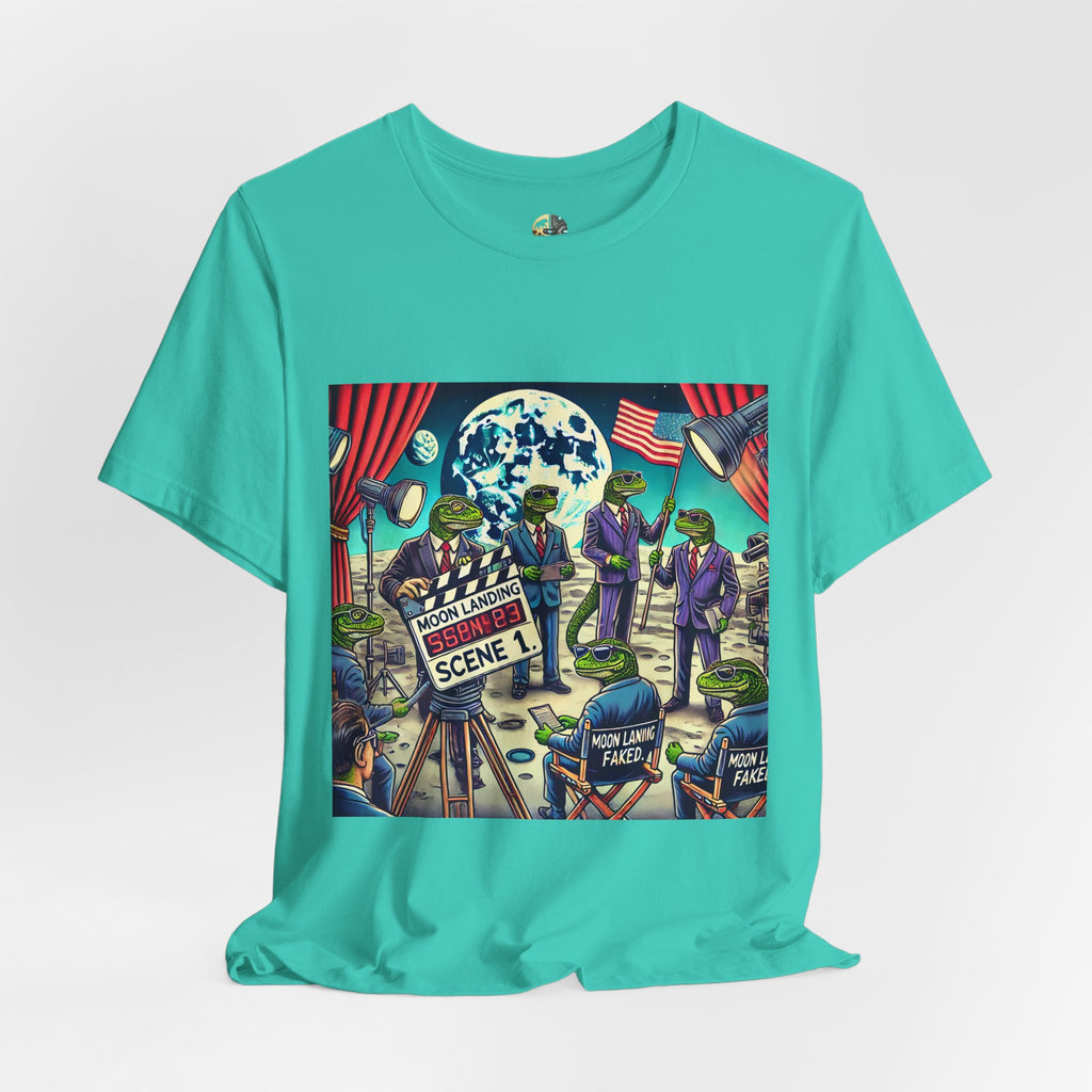 Teal T-shirt featuring a graphic of lizard people in suits on a movie set staging a moon landing scene, with studio lights and a clapperboard