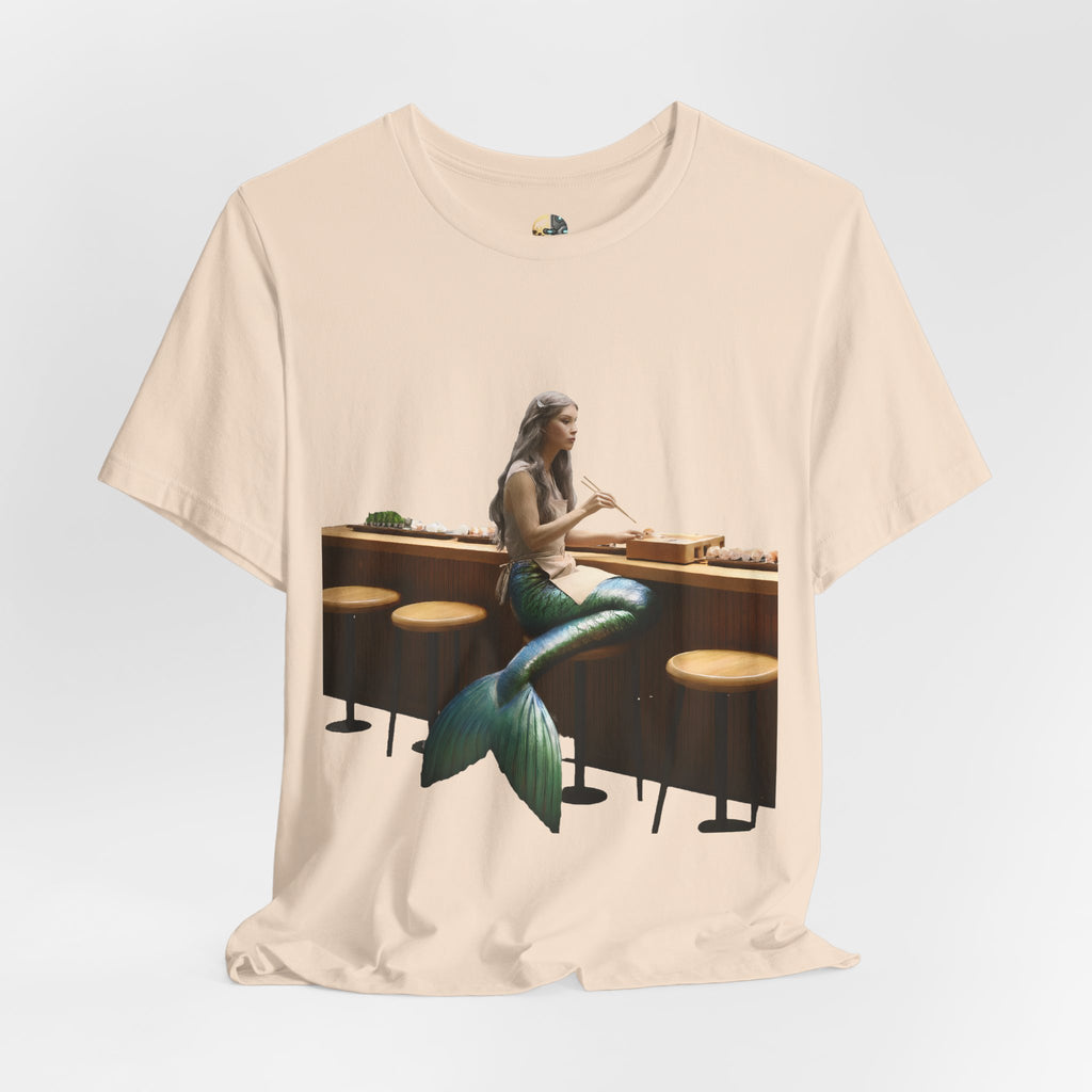 Soft creme T-shirt with graphic of a mermaid wearing a chef’s apron sitting at a sushi bar and eating sushi with chopsticks