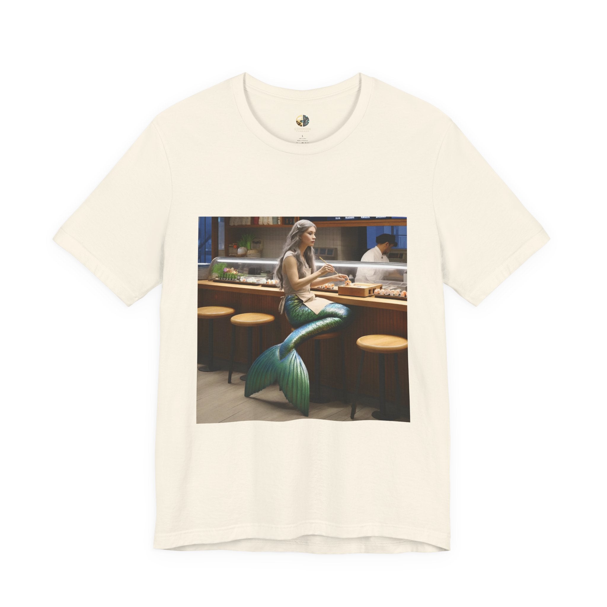 Natural color T-shirt featuring a graphic of a mermaid wearing a chef’s apron sitting at a sushi bar and eating sushi, with a chef behind the counter