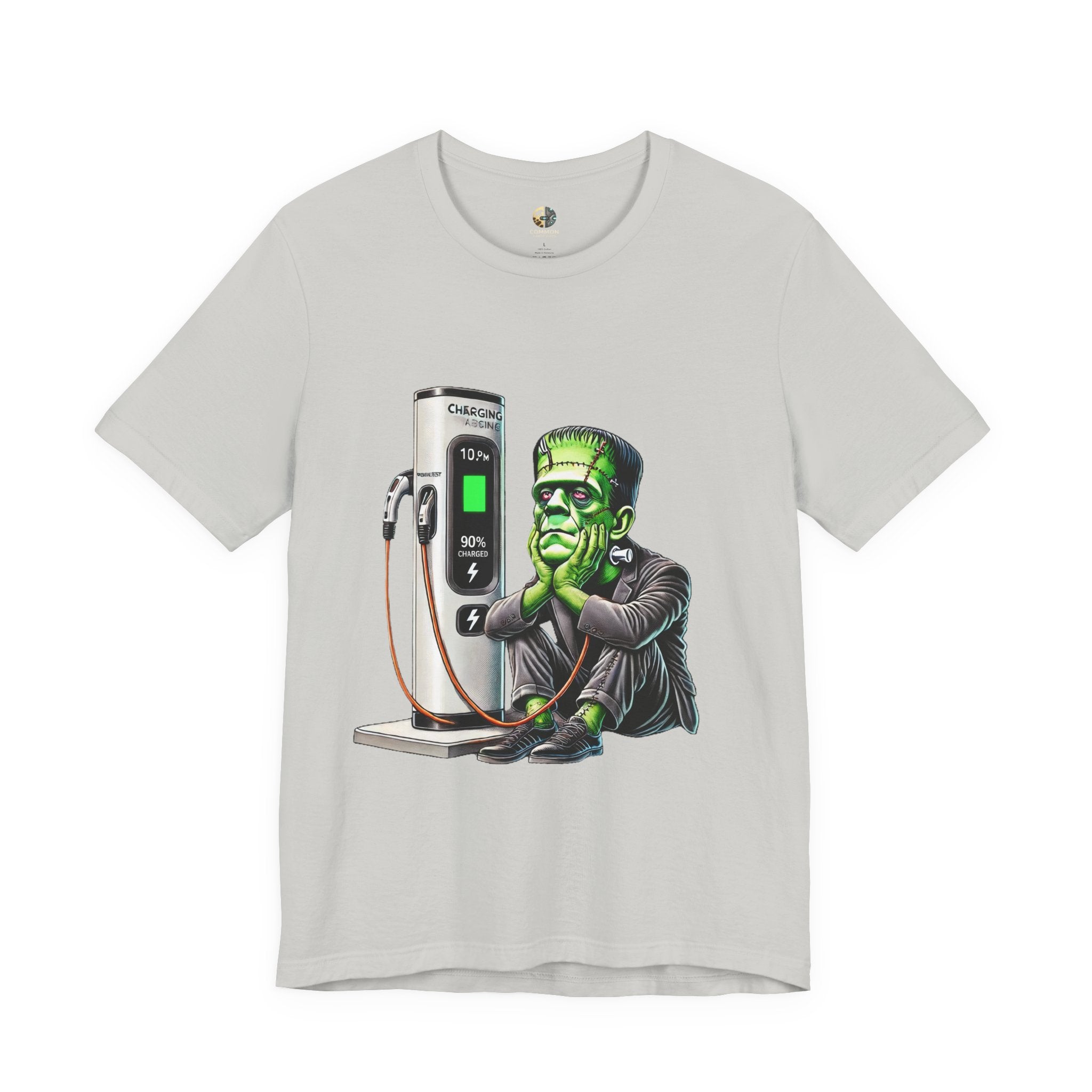 Silver T-shirt featuring a graphic of Frankenstein’s monster sitting at an electric charging station, plugged in and waiting for the charge to complete
