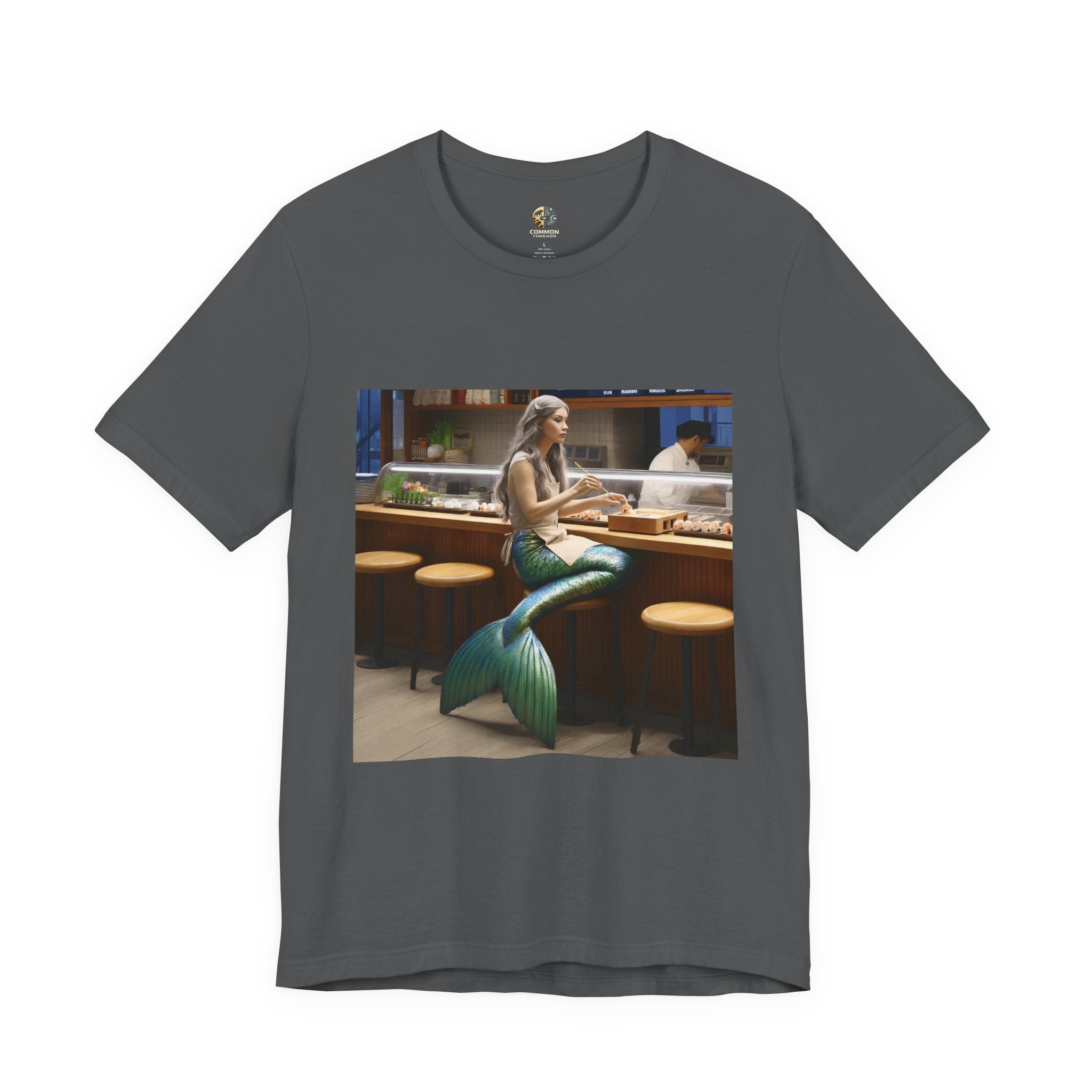 Asphalt grey T-shirt featuring a graphic of a mermaid wearing a chef’s apron sitting at a sushi bar and eating sushi, with a chef behind the counter