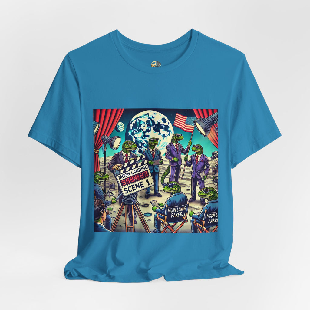 Aqua blue T-shirt featuring a graphic of lizard people in suits on a movie set staging a moon landing scene, with studio lights and a clapperboard