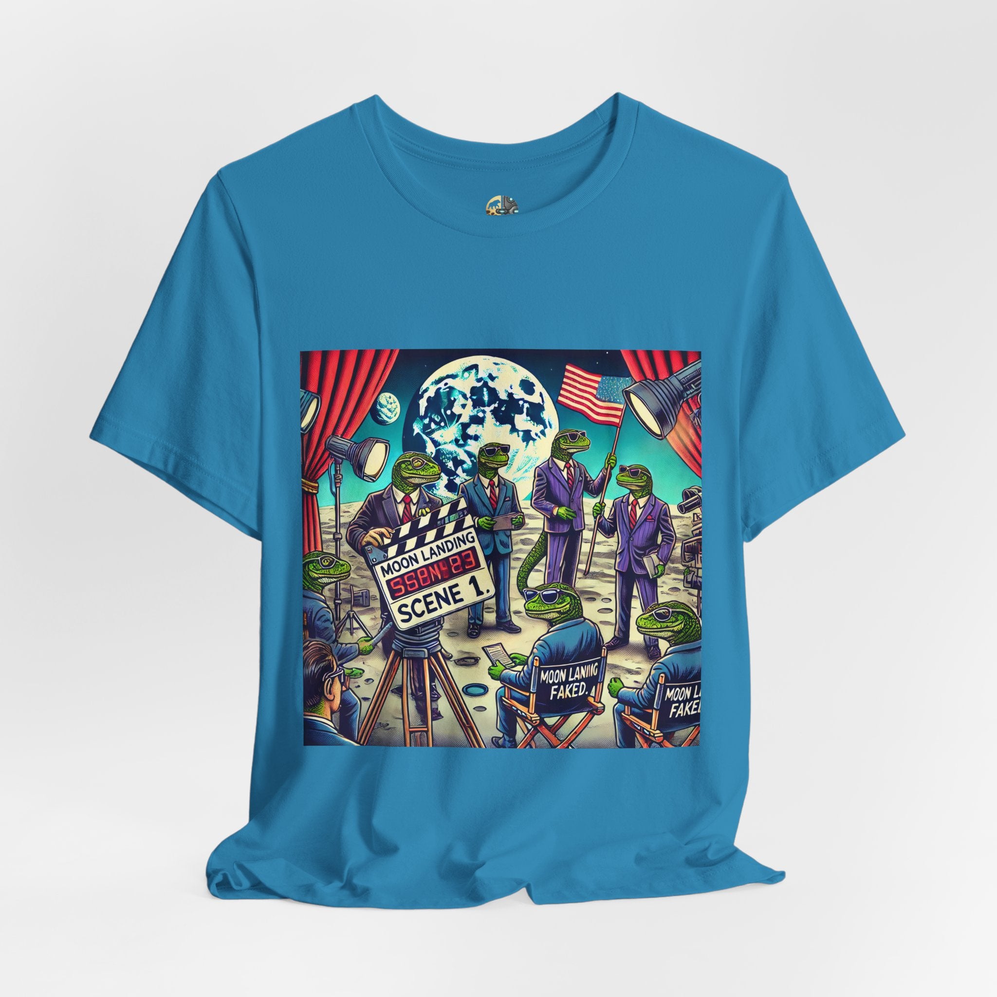 Aqua blue T-shirt featuring a graphic of lizard people in suits on a movie set staging a moon landing scene, with studio lights and a clapperboard