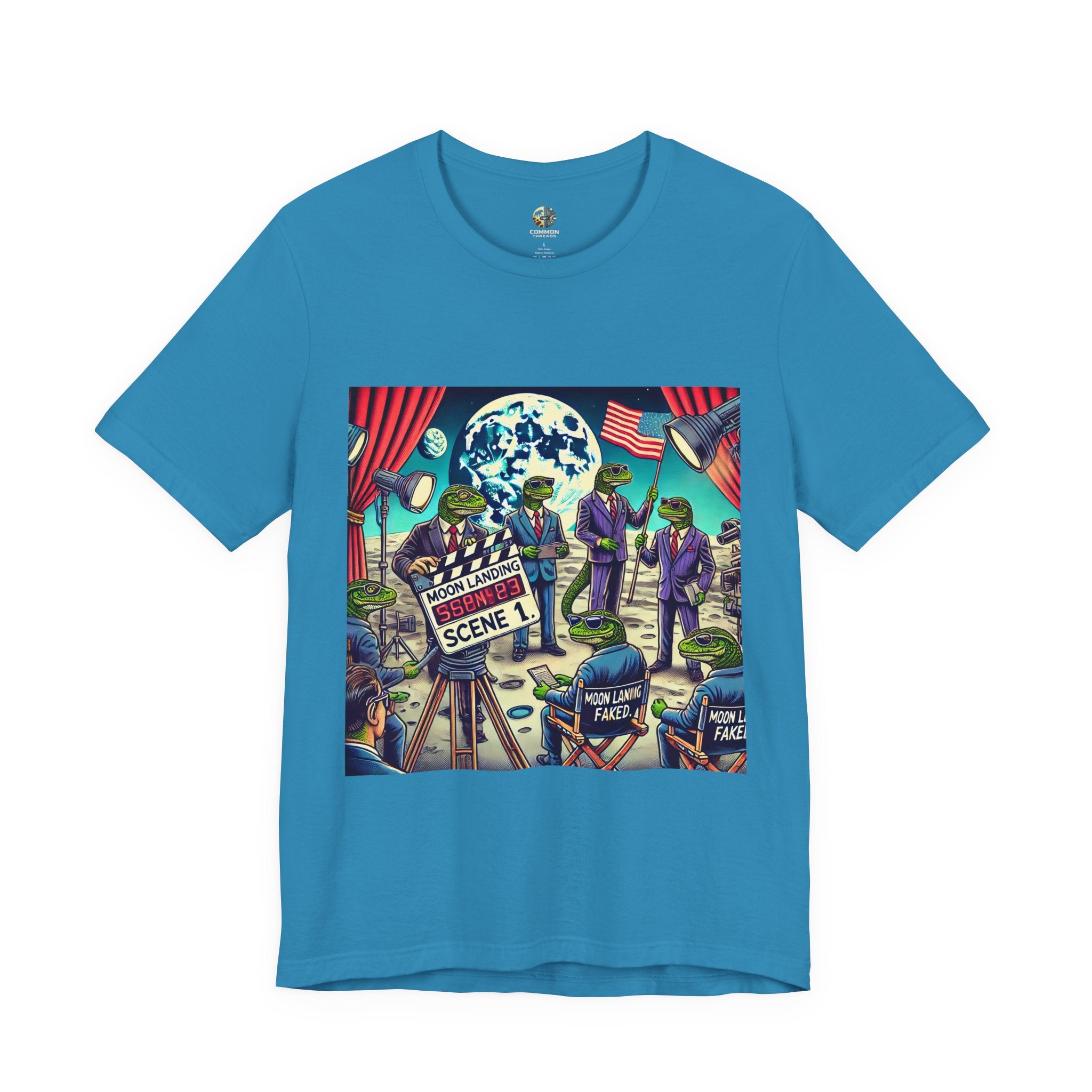 Aqua blue T-shirt featuring a graphic of lizard people in suits on a movie set staging a moon landing scene, with studio lights and a clapperboard