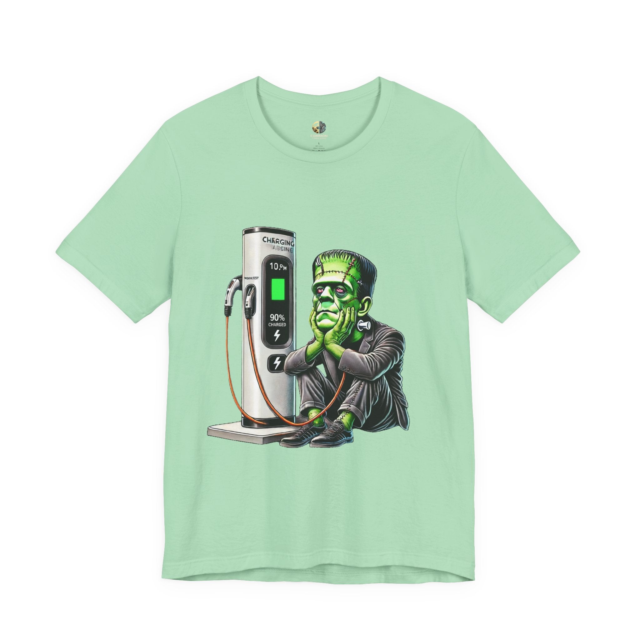 Mint green T-shirt featuring a graphic of Frankenstein’s monster sitting at an electric charging station, plugged in and waiting for the charge to complete