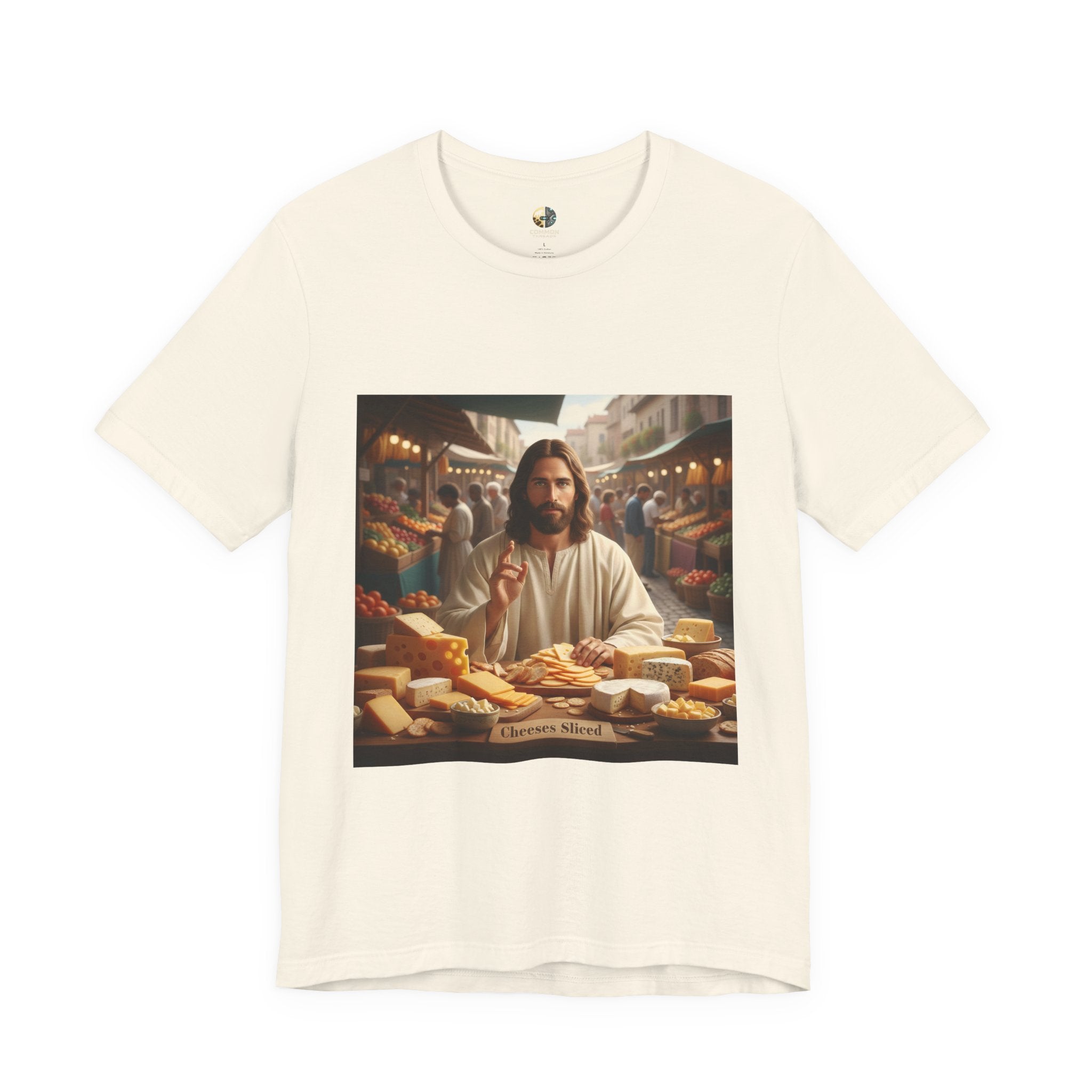 Natural color T-shirt featuring a graphic of Jesus in traditional robes at an ancient marketplace selling assorted cheeses, with a sign reading ‘Cheeses Sliced‘