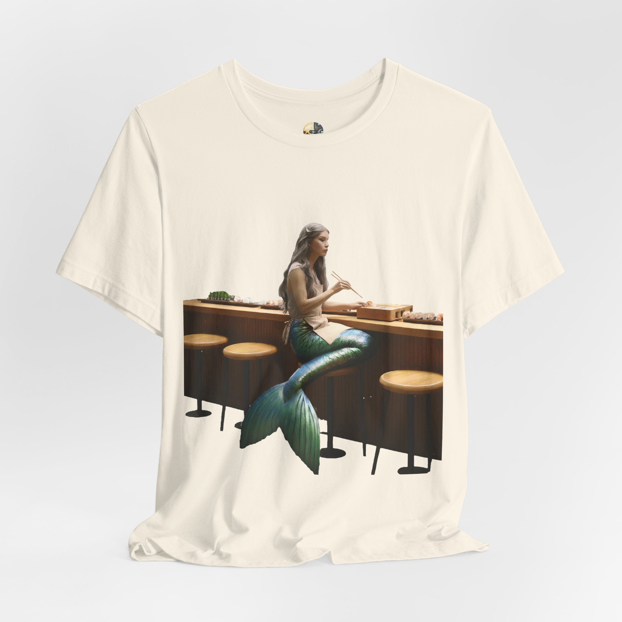 Natural color T-shirt with graphic of a mermaid wearing a chef’s apron sitting at a sushi bar and eating sushi with chopsticks