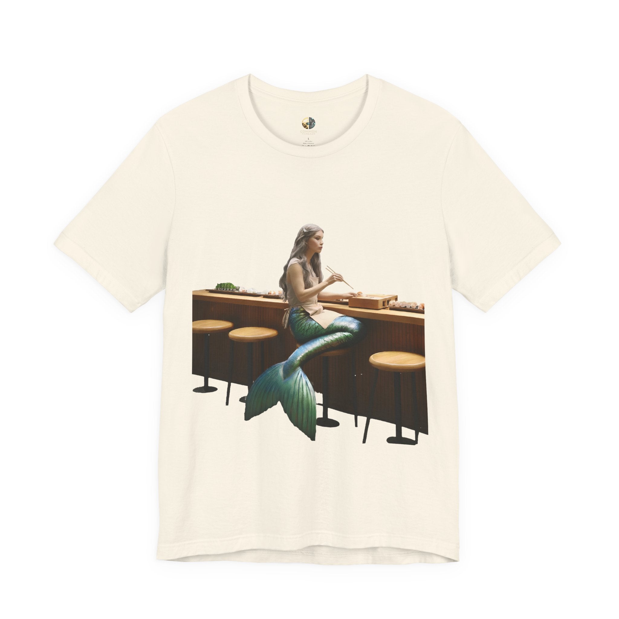 Natural color T-shirt with graphic of a mermaid wearing a chef’s apron sitting at a sushi bar and eating sushi with chopsticks
