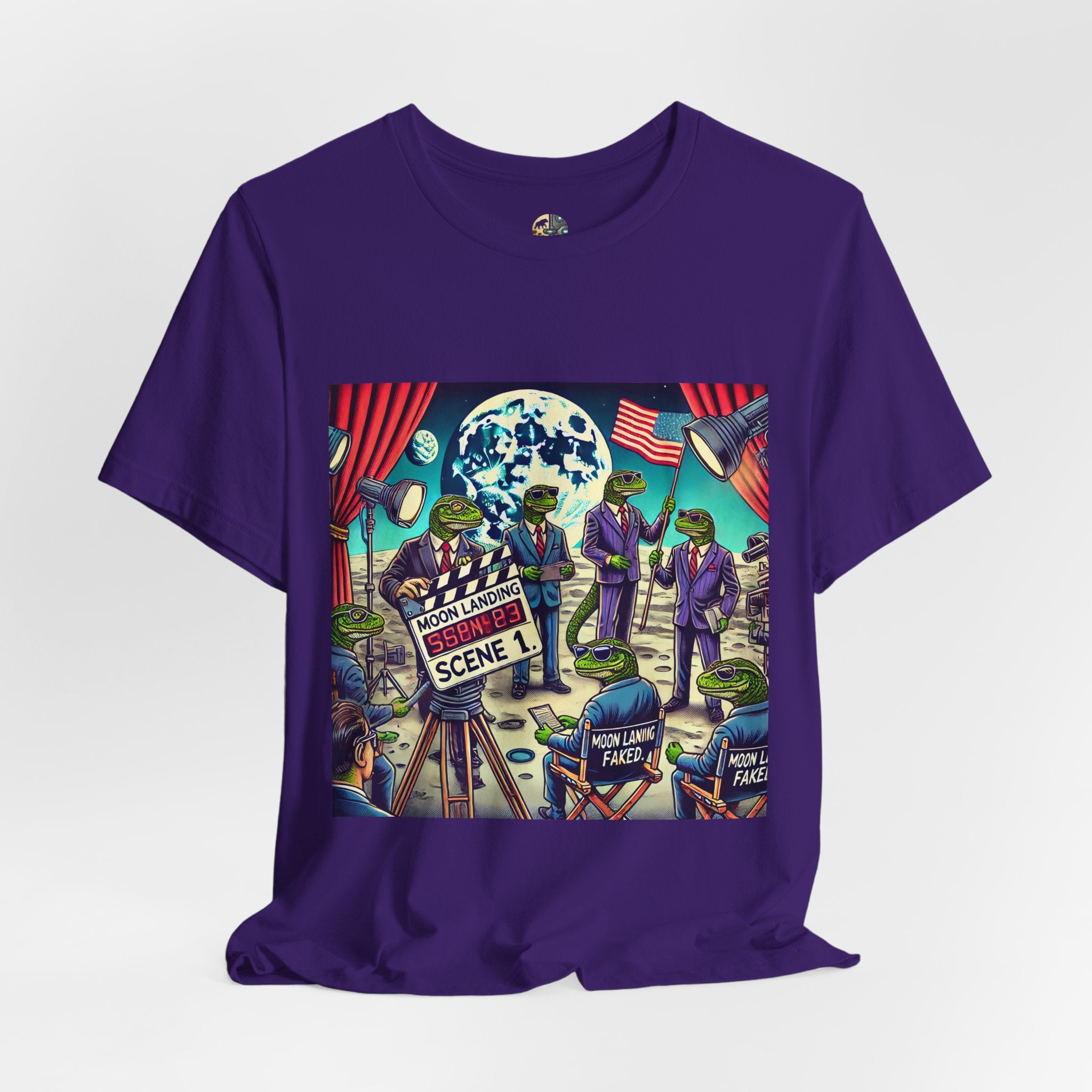 Purple T-shirt featuring a graphic of lizard people in suits on a movie set staging a moon landing scene, with studio lights and a clapperboard