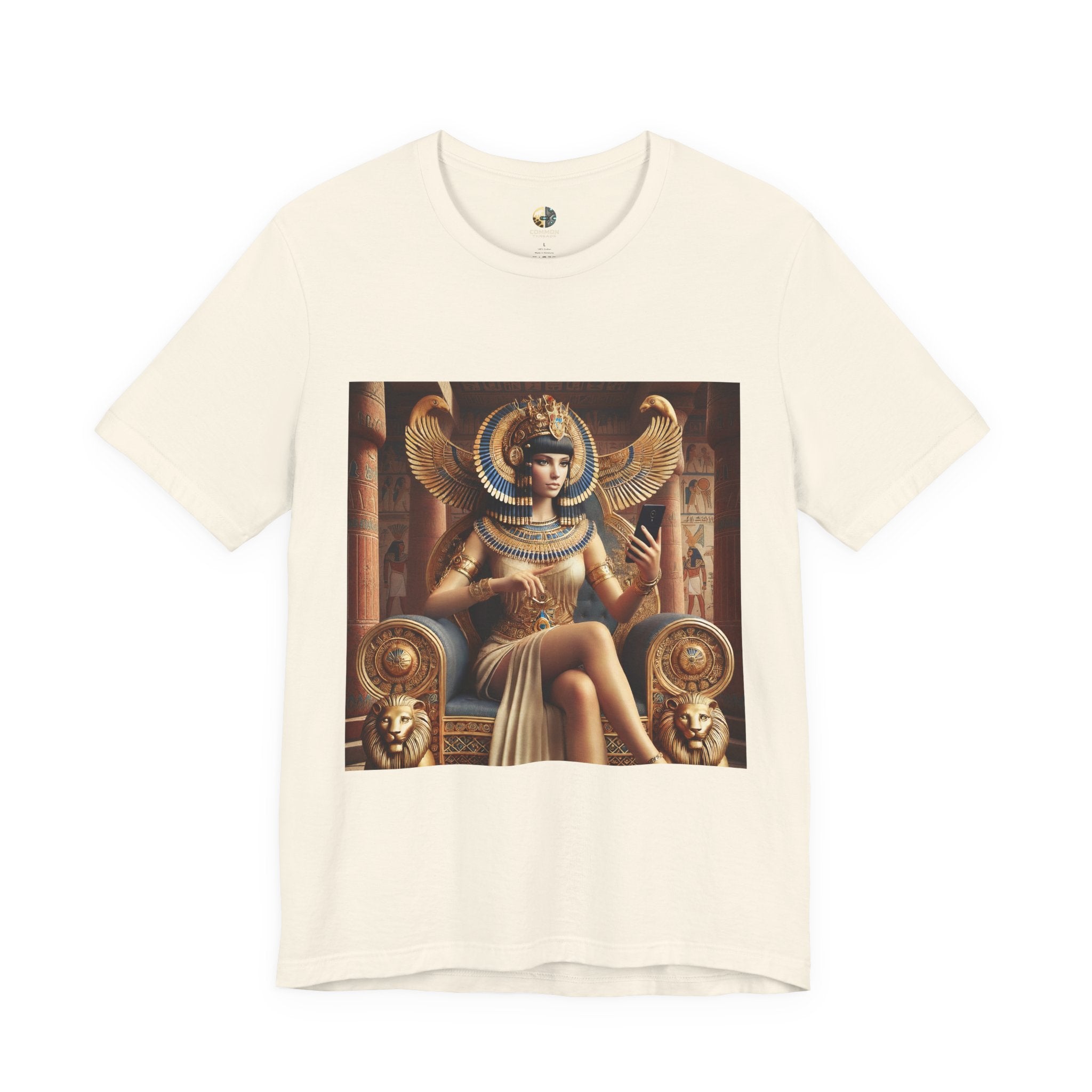 Natural color T-shirt featuring a graphic of Cleopatra wearing an ornate headdress and gold jewelry, seated on a throne and holding a smartphone for a selfie, with temple architecture in the background