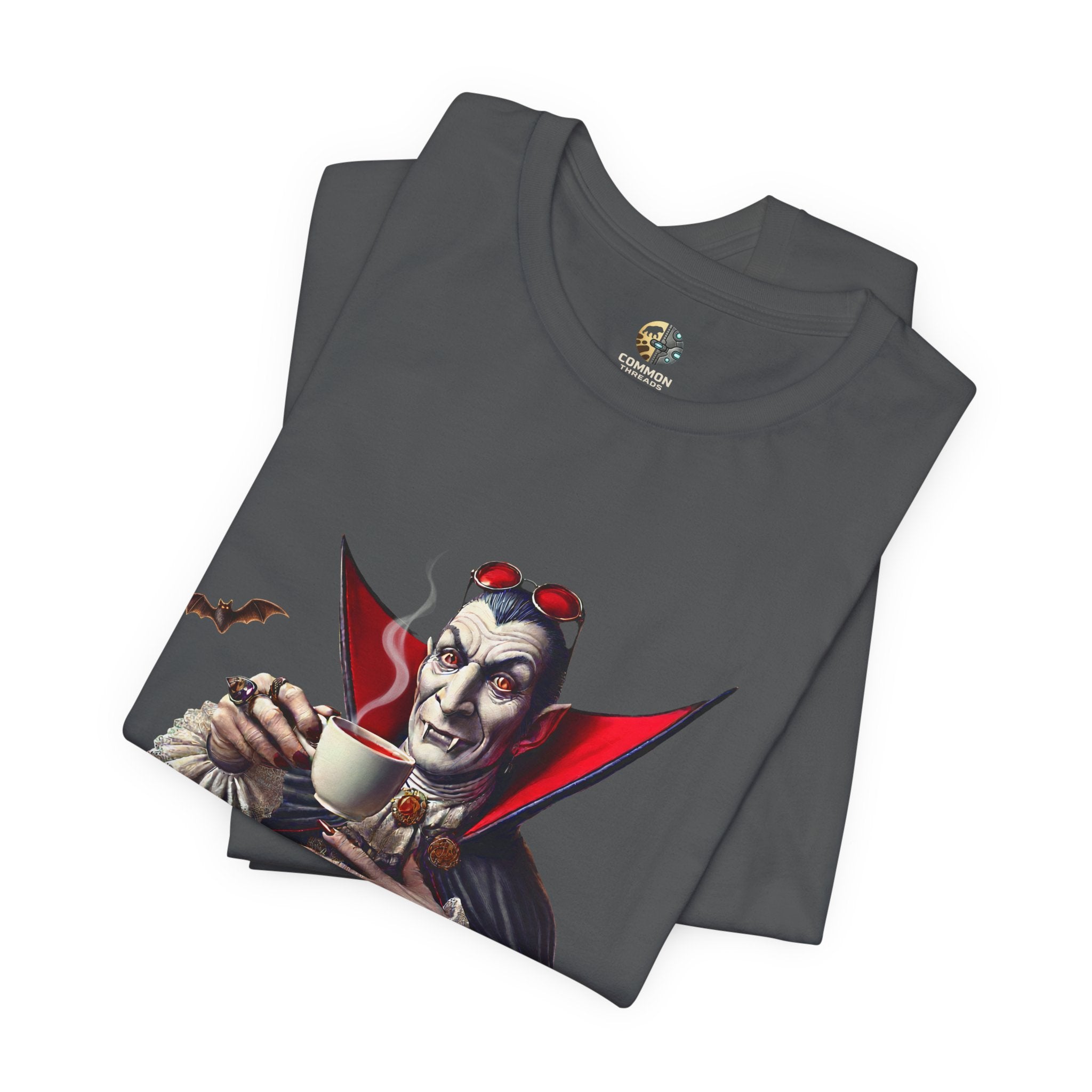 Folded asphalt grey T-shirt featuring a classic vampire dressed like Count Dracula sitting at a table, wearing red sunglasses and drinking from a teacup filled with red liquid