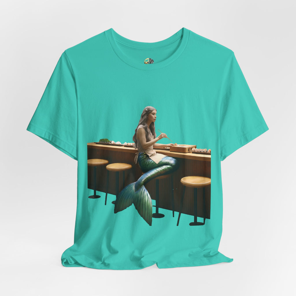 Teal T-shirt with graphic of a mermaid wearing a chef’s apron sitting at a sushi bar and eating sushi with chopsticks