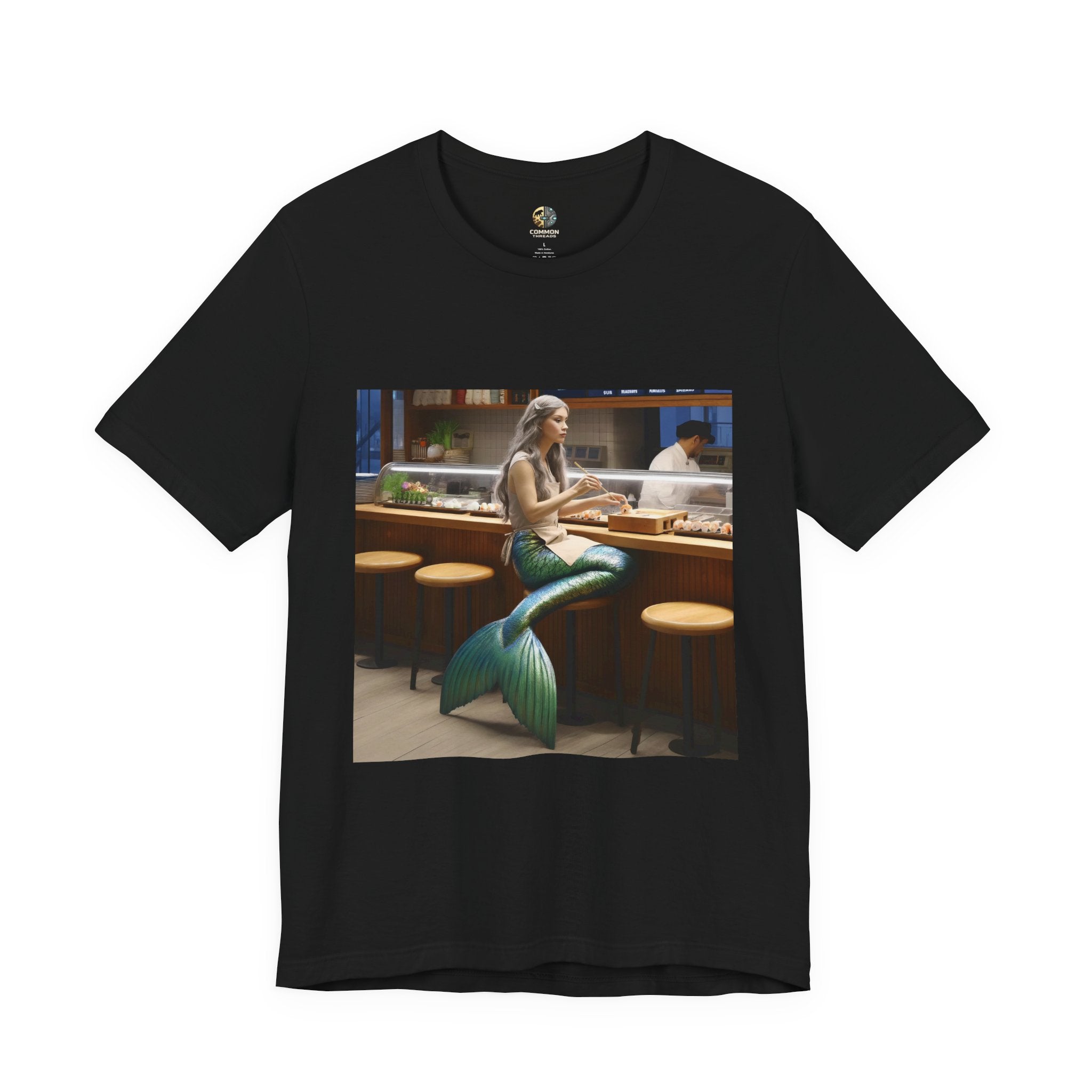 Black T-shirt featuring a graphic of a mermaid wearing a chef’s apron sitting at a sushi bar and eating sushi, with a chef behind the counter