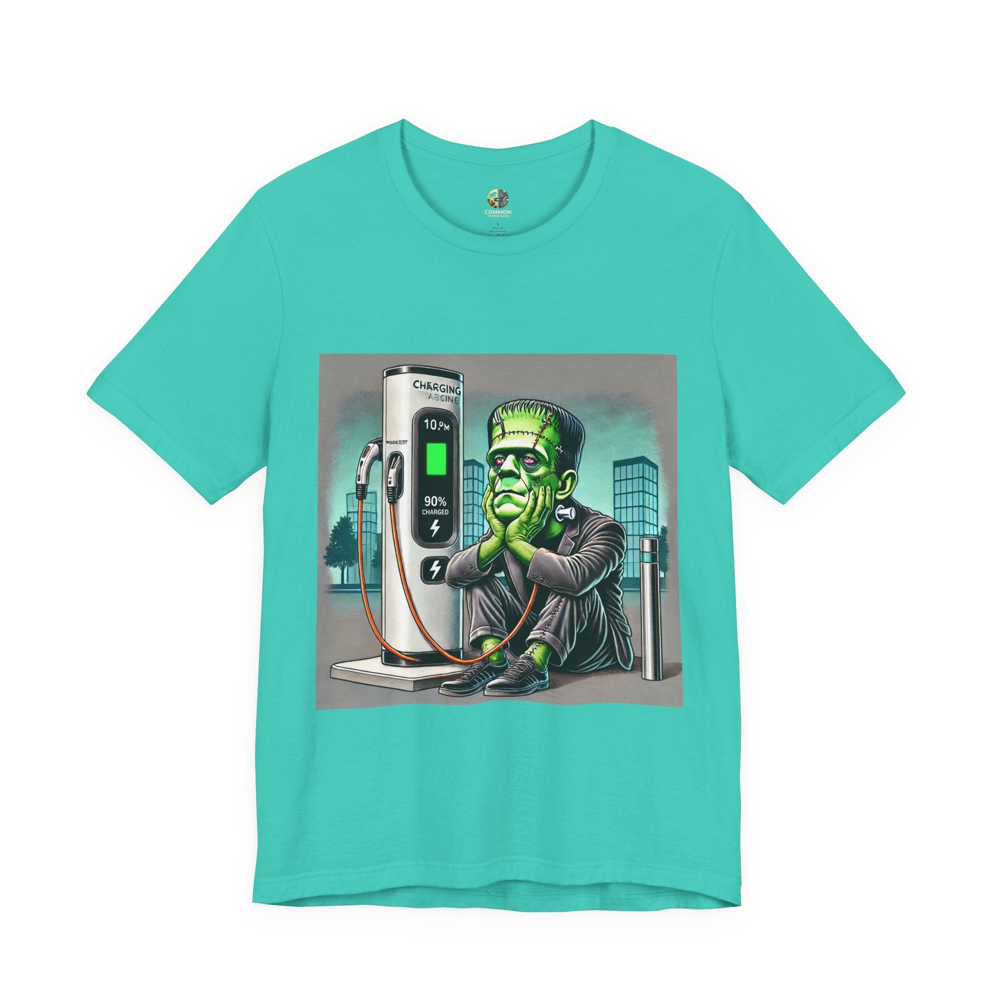 Teal T-shirt featuring a graphic of Frankenstein’s monster sitting at an electric charging station, plugged in and waiting for the charge to complete, with office buildings in the background