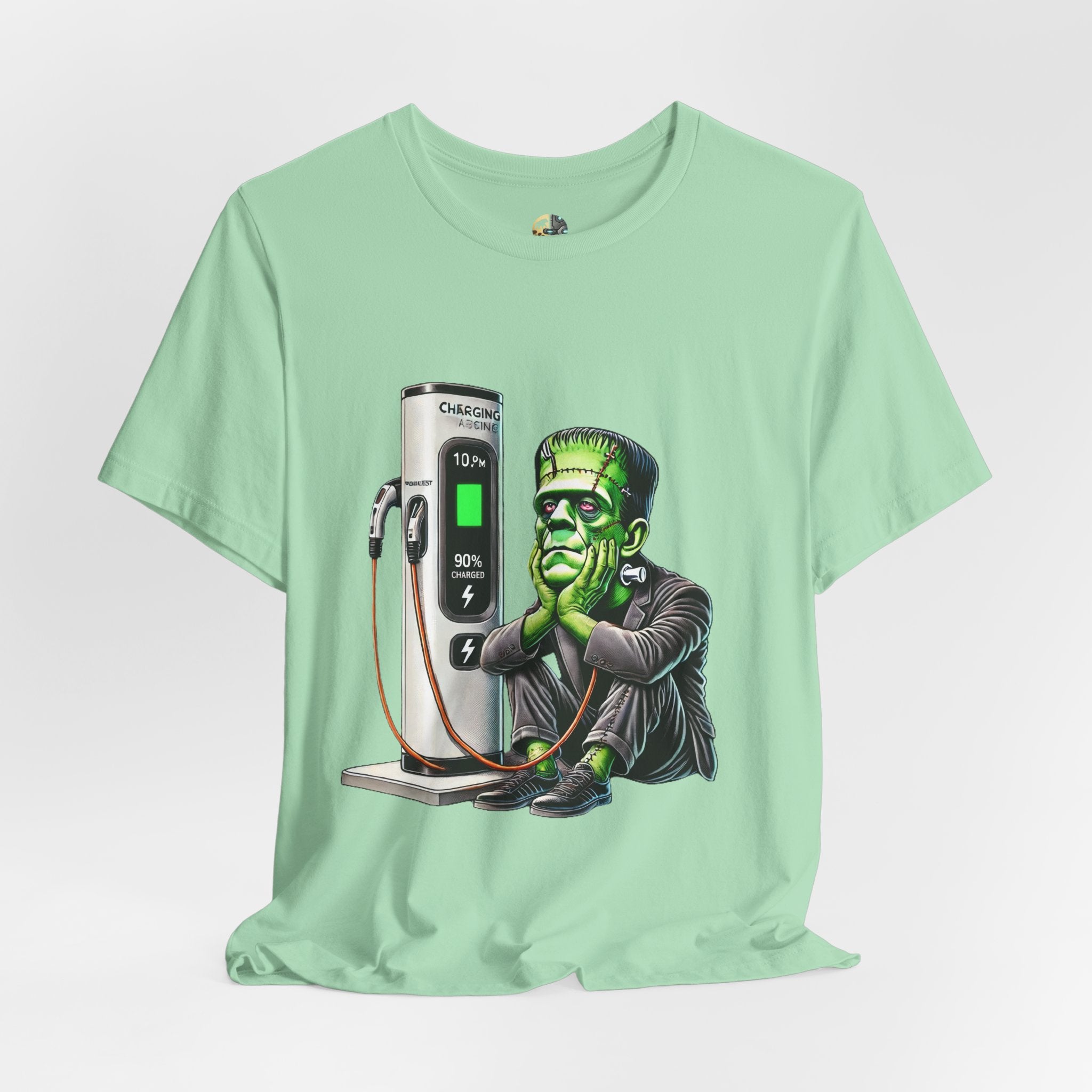 Mint green T-shirt featuring a graphic of Frankenstein’s monster sitting at an electric charging station, plugged in and waiting for the charge to complete