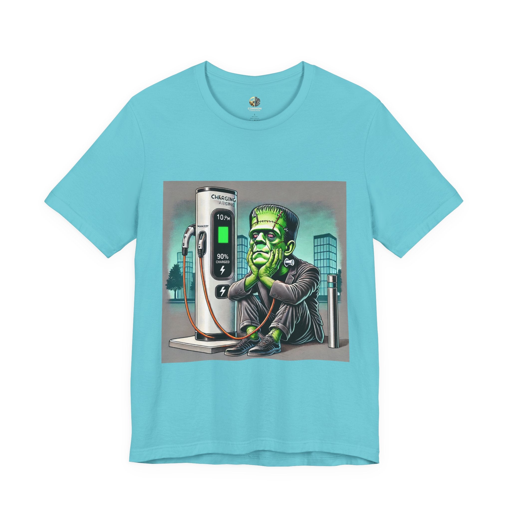 Turquoise T-shirt featuring a graphic of Frankenstein’s monster sitting at an electric charging station, plugged in and waiting for the charge to complete, with office buildings in the background