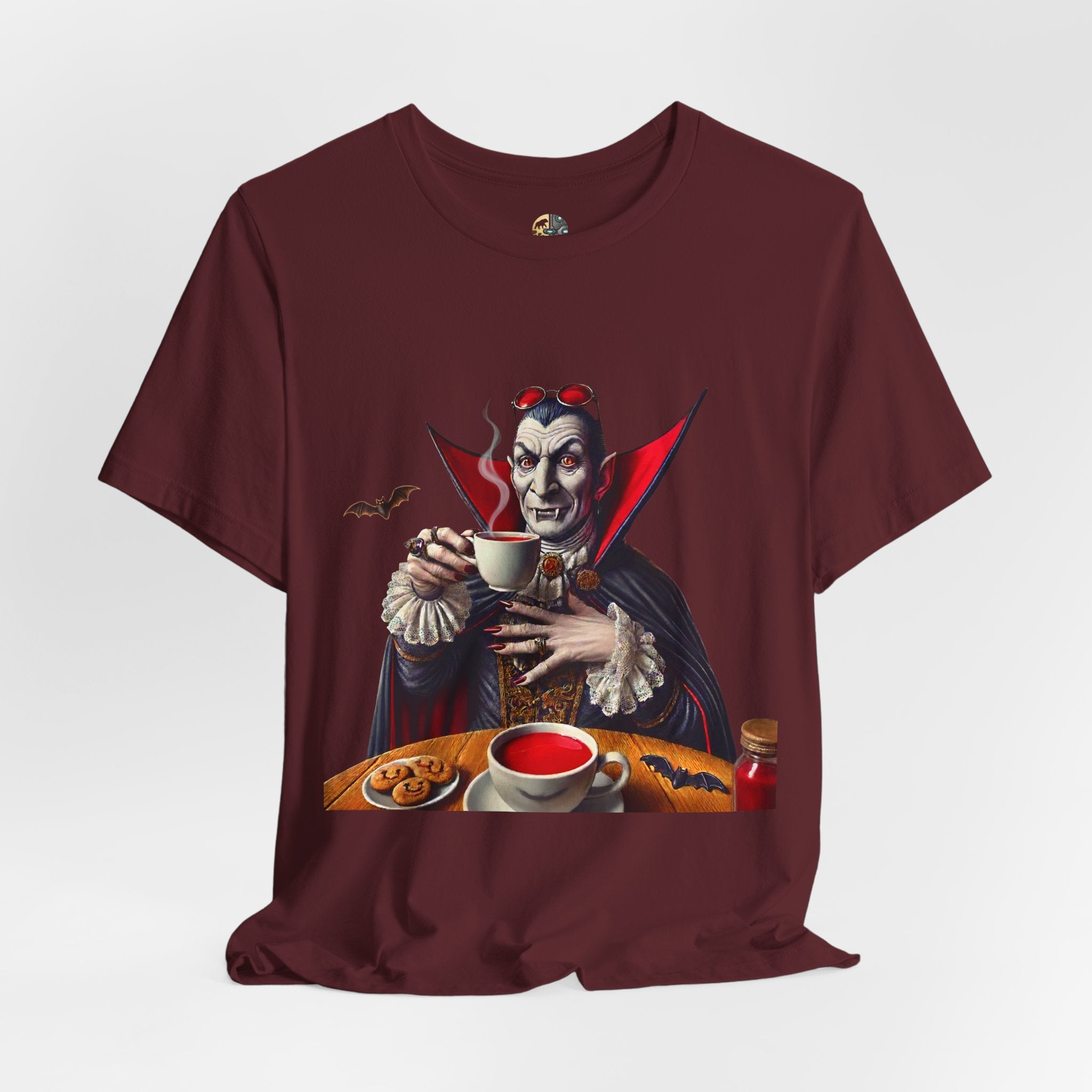 Maroon color T-shirt featuring a classic vampire dressed like Count Dracula sitting at a table, wearing red sunglasses and drinking from a teacup filled with red liquid