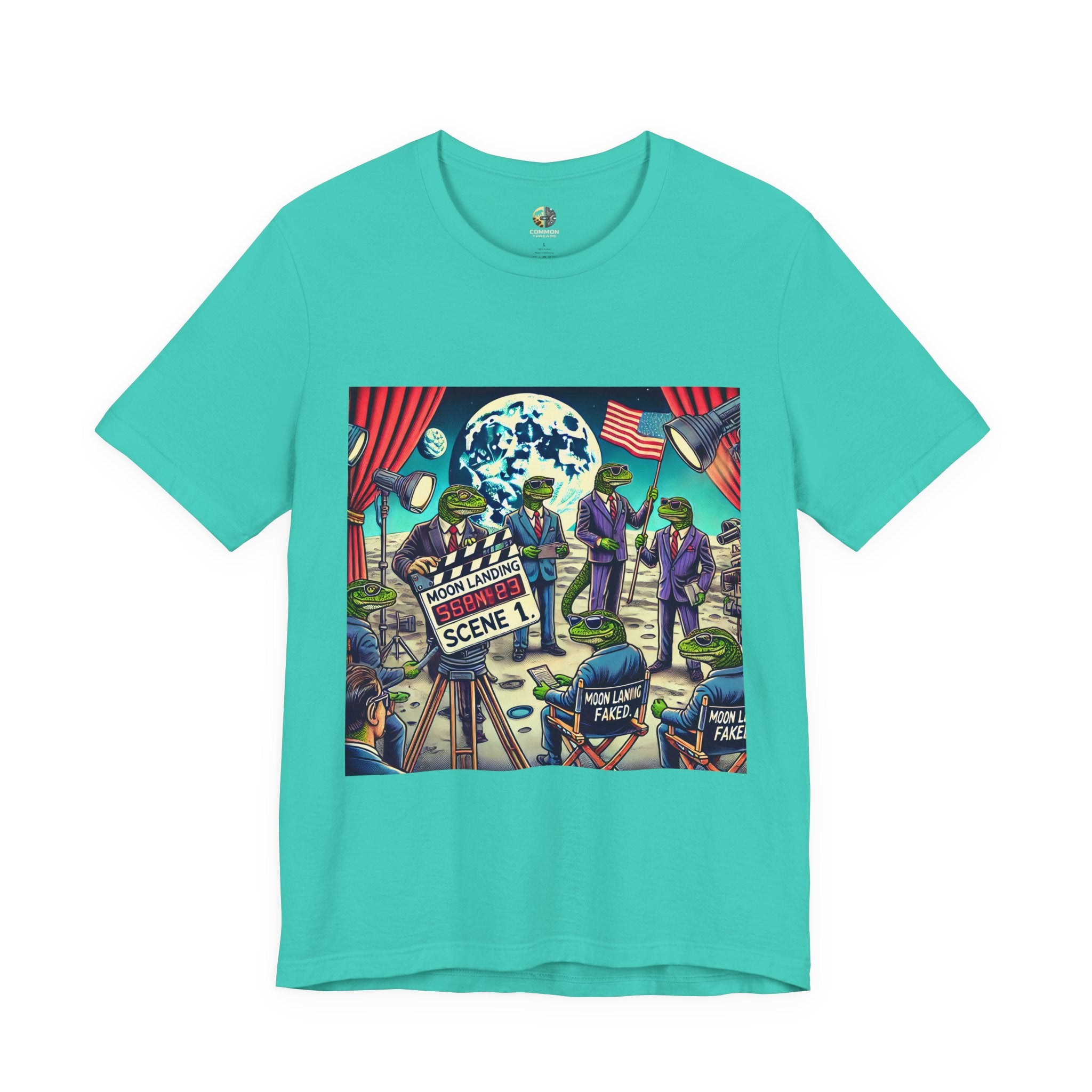 Teal T-shirt featuring a graphic of lizard people in suits on a movie set staging a moon landing scene, with studio lights and a clapperboard