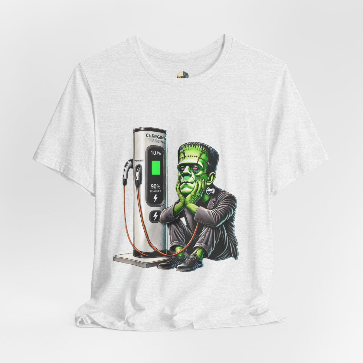 Ash color T-shirt featuring a graphic of Frankenstein’s monster sitting at an electric charging station, plugged in and waiting for the charge to complete